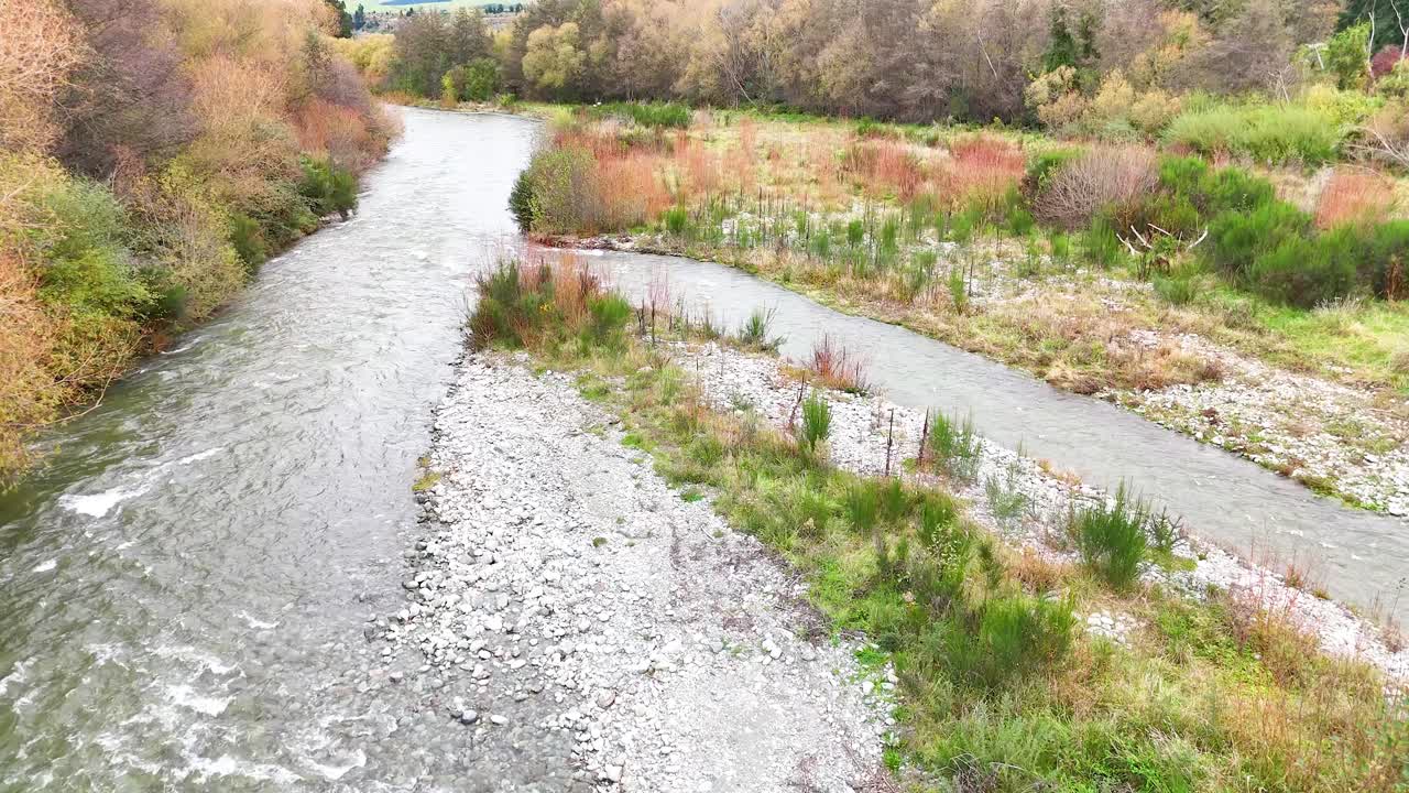 A tranquil river meanders through lush greenery under soft daylight, captured in a smooth aerial sequence