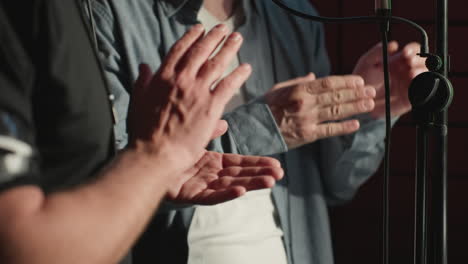 close-up of two people clapping hands expressively in a soundproof recording studio, mid-performance in front of a microphone stand. the focus is on their movements and the studio environment