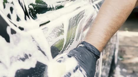 close up of a male washing a car wearing a black gloves with shampoo and sponge