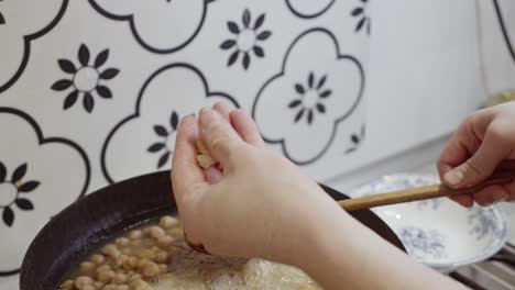 chef stirs pan full of boiling chickpeas and checks them for cooking quality by mashing with his hand