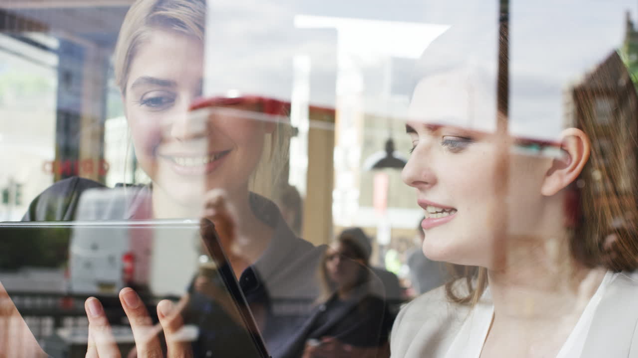 두 여자 친구가 카페에서 디지털 태블릿을 사용하여 커피를 나누고 있습니다.