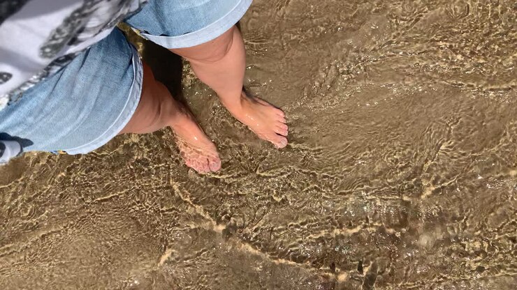 Una donna si bagna i piedi nel mare, dolci onde accarezzano le gambe della ragazza, la sabbia dorata scintilla al sole.