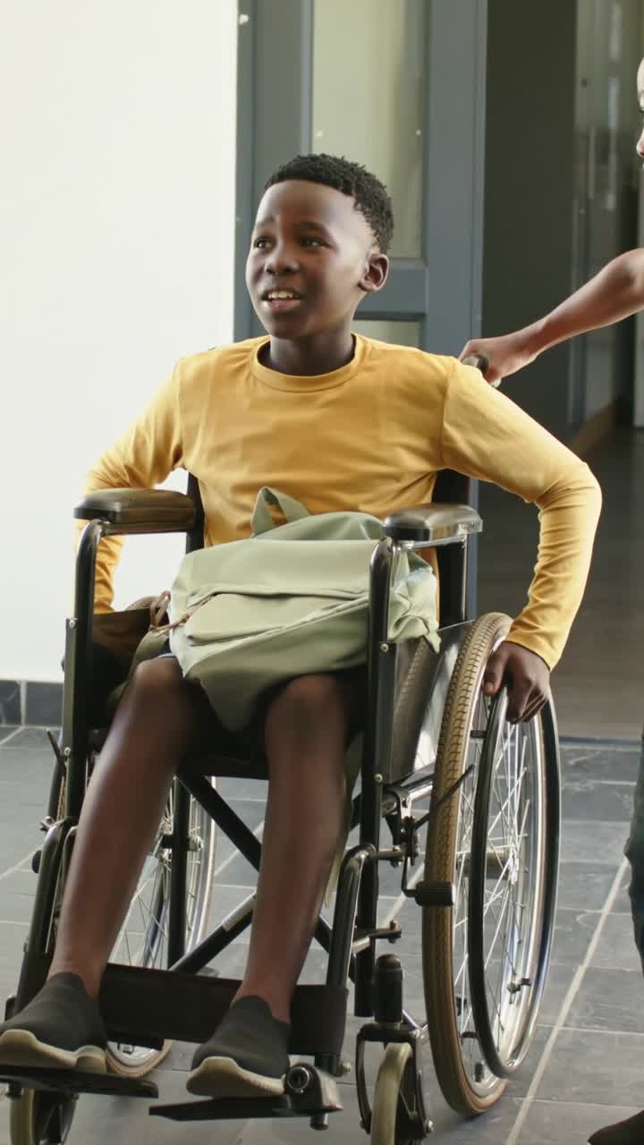 Vertical video: Hand pushing youth in yellow touching wheel, wheeling into hall with green backpack