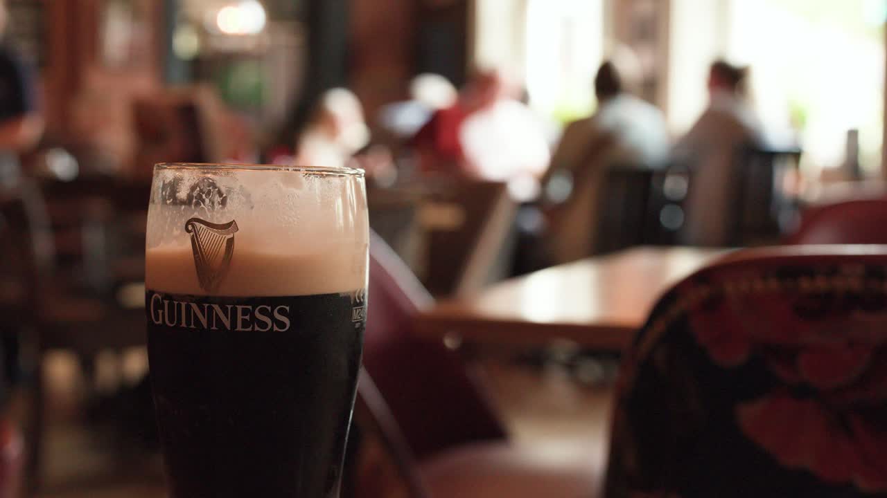 Pint of dark beer in focus, pub interior, shallow depth of field, warm lighting