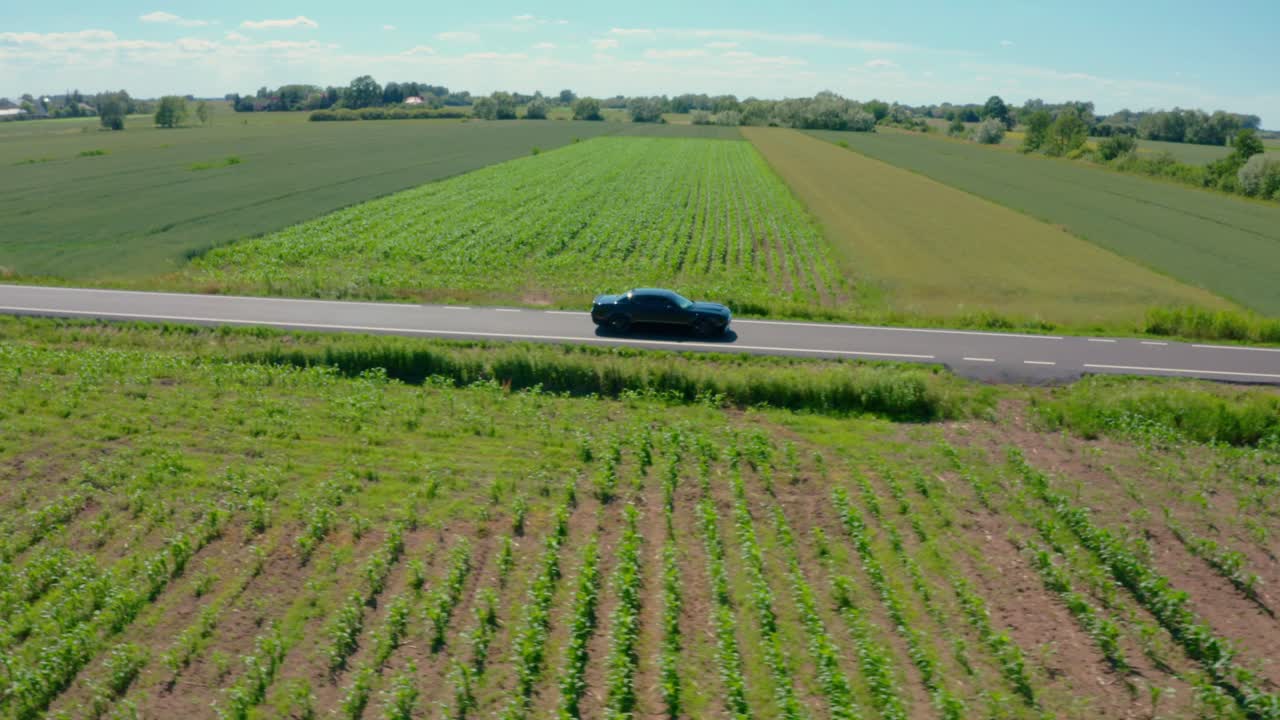 A dynamic drone shot pulling away from a Dodge Challenger Scat Pack driving along a rural road through picturesque farmland. Ideal for automotive, travel, and nature content.