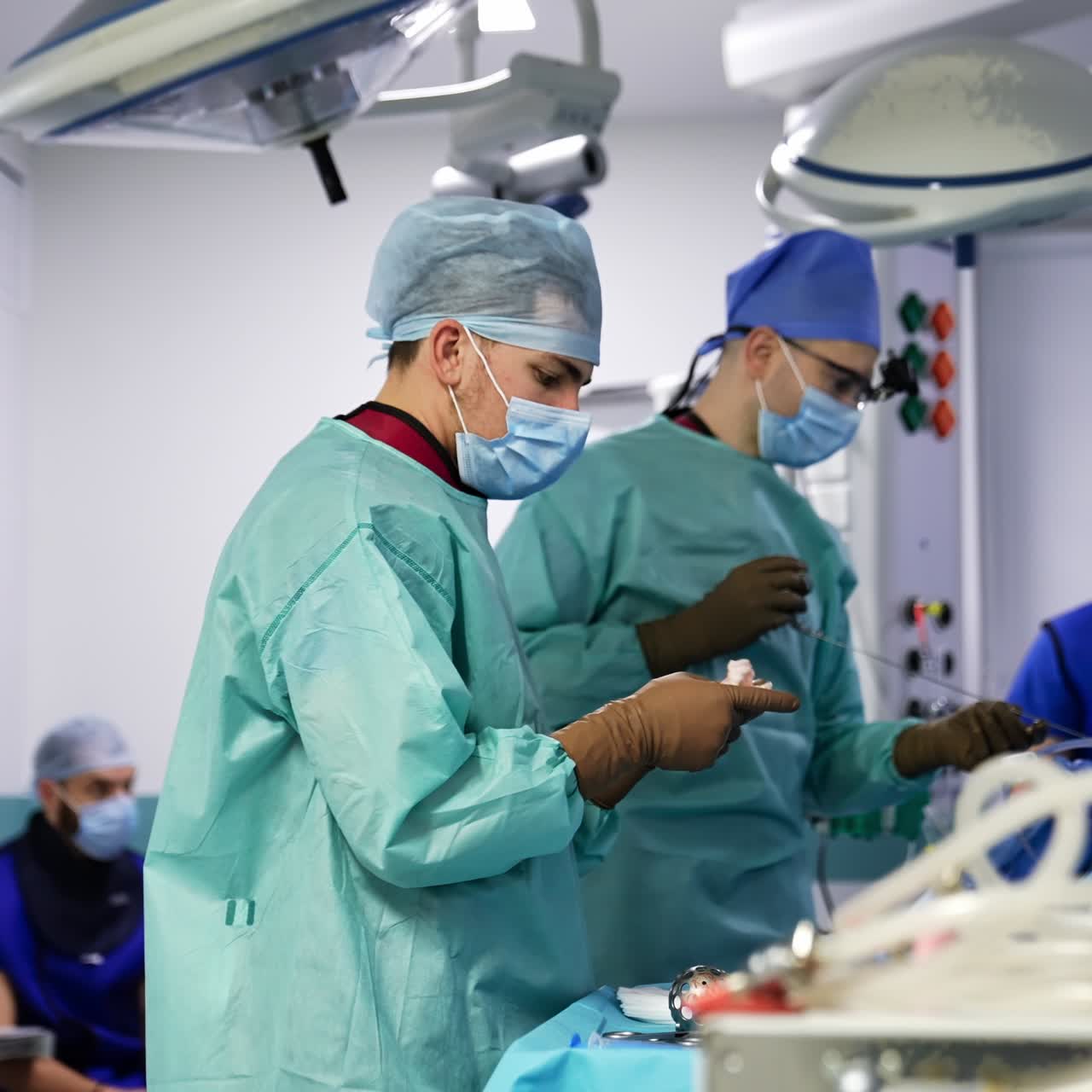 Chief surgeon pulls the long needle instrument out from a patient. Assistant cleans the tool quickly