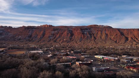 Flying-away-from-the-red-rock-canyon-wall-in-Moab-Utah-during-golden-hour,-aerial