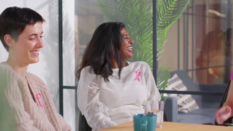 smiling mature woman wearing pink breast cancer awareness ribbon talking at meeting of therapy support group for cancer treatment patients 1