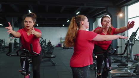 Group-of-girls-performs-aerobic-training-workout-cardio-routine-on-bike-simulators,-cycle-training