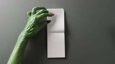 Video-of-halloween-green-monster-hands-and-notebook-with-copy-space-on-grey-background