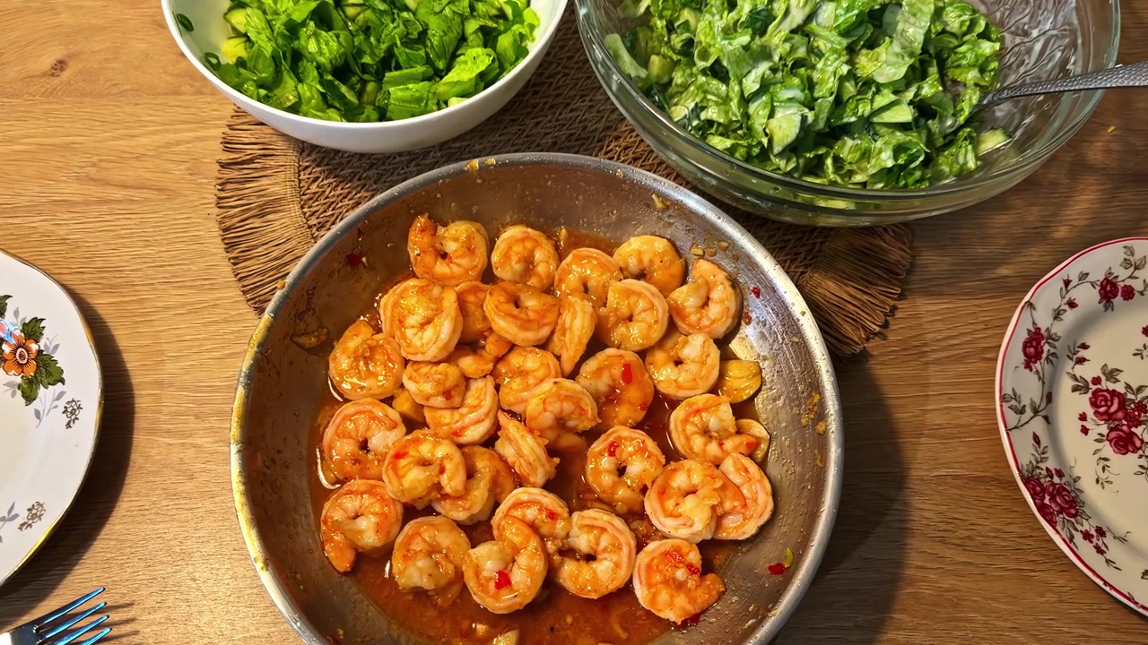 Gamberi cotti in salsa serviti con insalate verdi fresche su un tavolo da pranzo in legno.