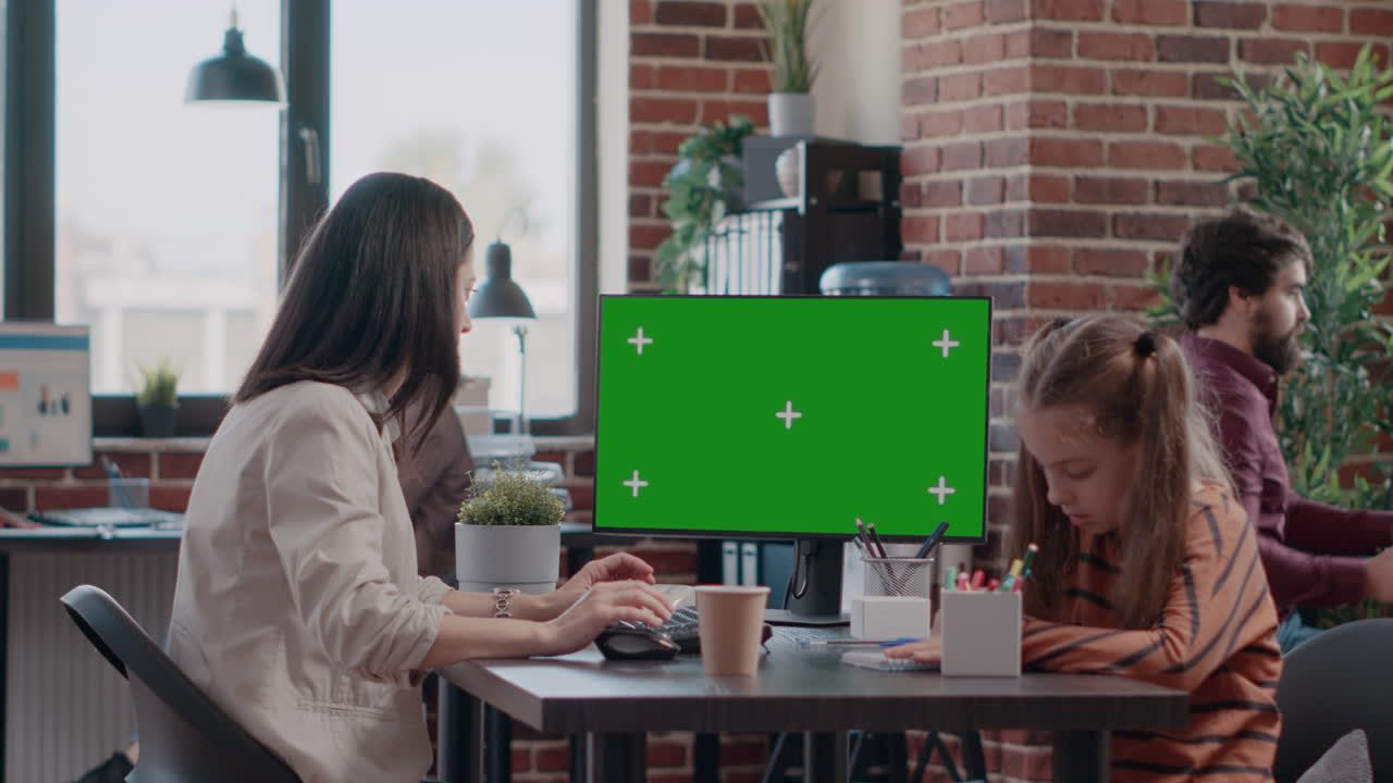 Working mother using horizontal green screen on computer and little girl doodling