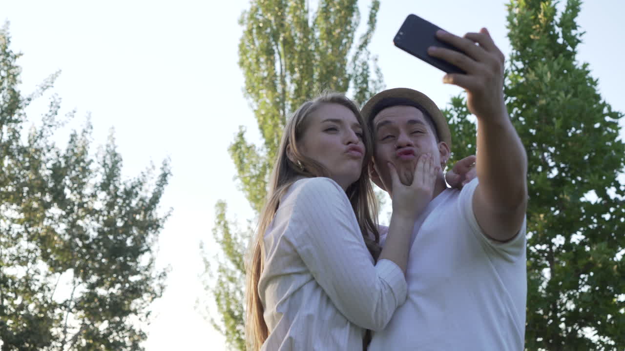 Young couple taking a selfie on their mobile in the park. Latin man and Caucasian woman
