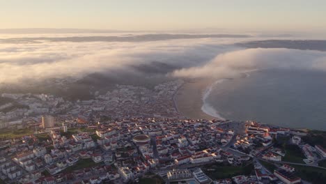 Nubes-Bajas-Rodando-Sobre-La-Costa-En-Nazare-Portugal-Durante-El-Amanecer,-Antena