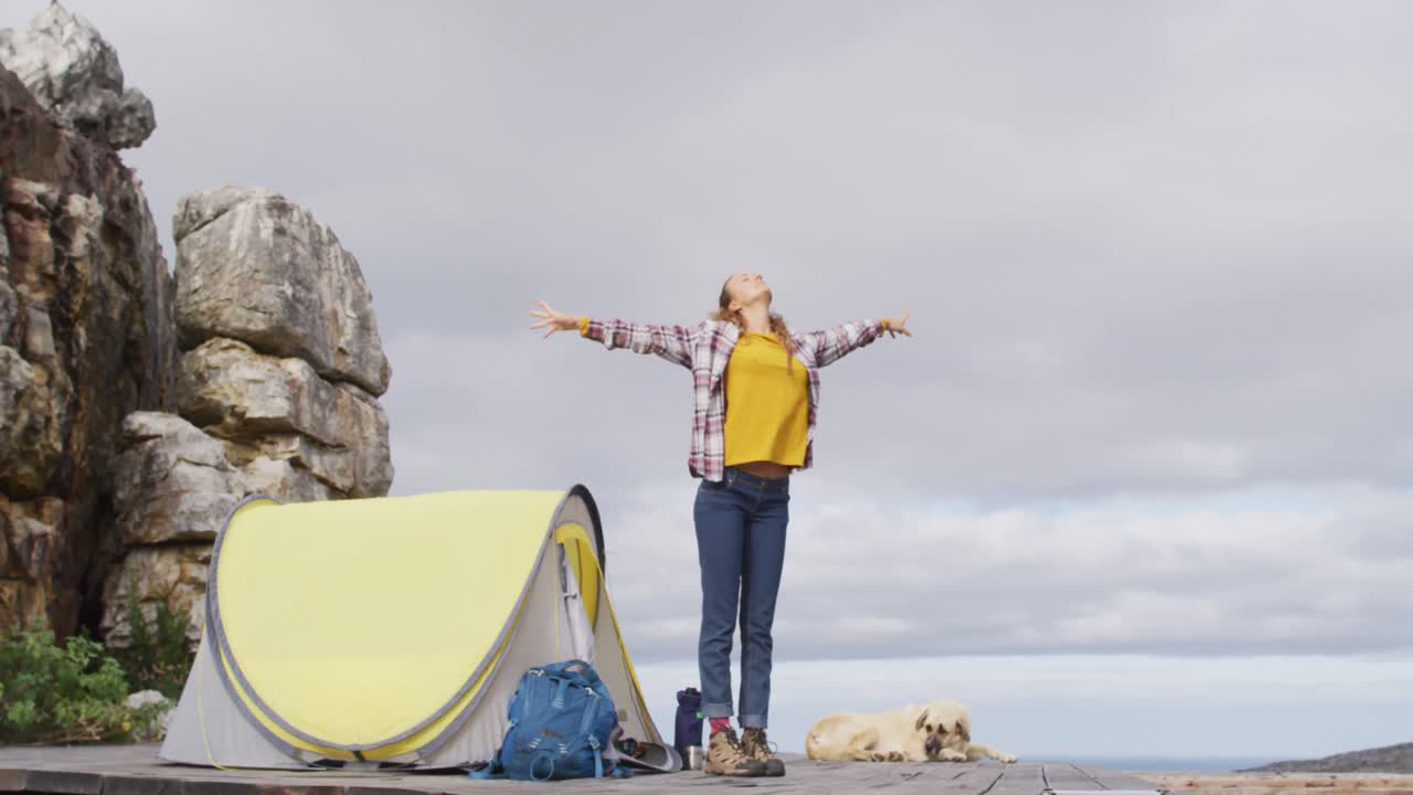mujer caucásica acampando, de pie y estirándose en la ladera de la montaña rural