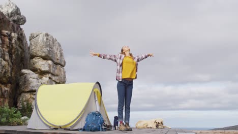 mujer caucásica acampando, de pie y estirándose en la ladera de la montaña rural
