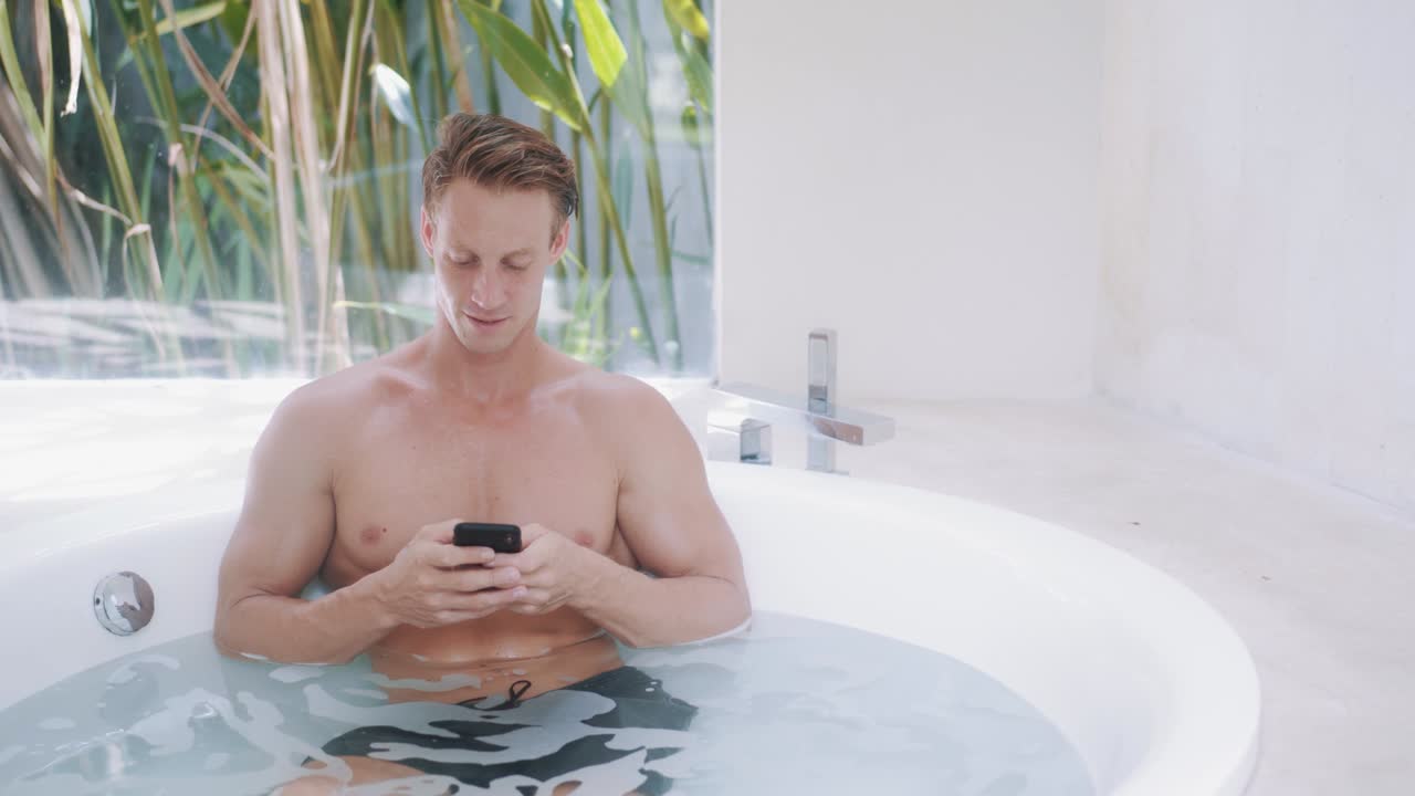 joven lee mensajes en su teléfono inteligente en una bañera moderna