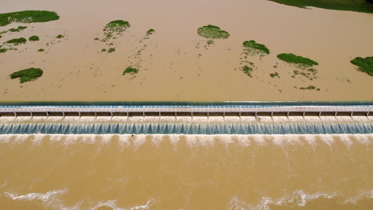 Dam With Muddy Water Flowing Over Its Crest, Creating A Waterfall-like Effect. - aerial shot