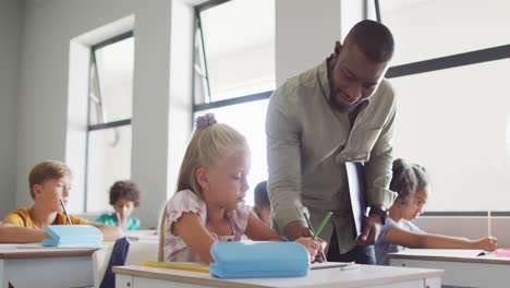 Video-of-happy-african-american-male-teacher-helping-in-exercise-to-caucasian-girl