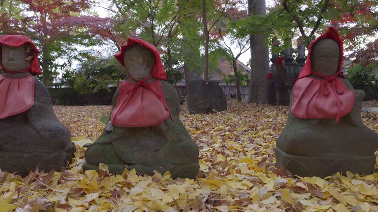 Typical Japanese Jizo statues on temple grounds with fallen autumn leafs