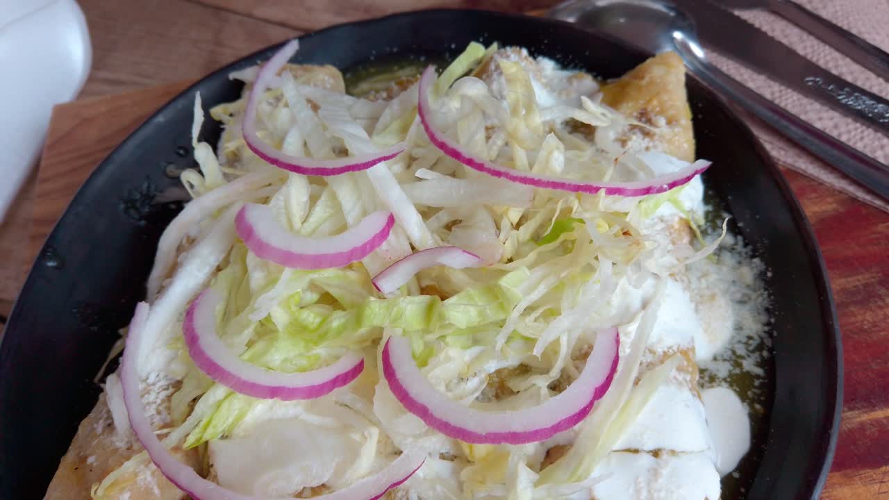 Overhead shot zooming out from a plate of Mexican enchiladas verdes, topped with lettuce, onion, and cheese.
