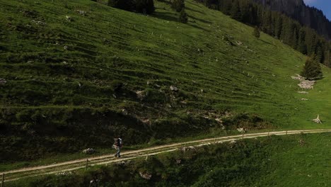 Aerial-drone-shot,-backpacker-hiking-on-mountain-cliffside-dirt-trail-during-summer