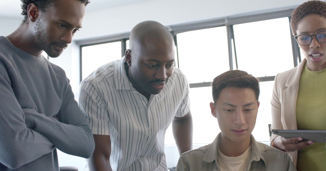 Diverse team in blazers reviewing as seated African man showing on laptop, woman pointing tablet