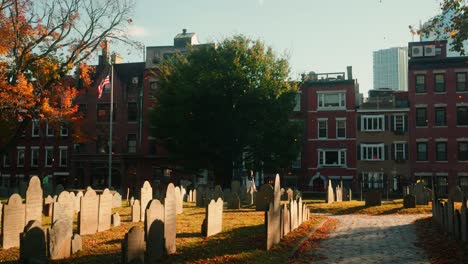 static shot of copps hill burying ground in boston during fall with graves in the foreground and a us flag in the background and fallen leaves, massachusetts, united states of america