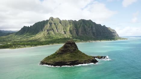 drone shot approaching chinaman's hat with the kualoa mountain range in the background