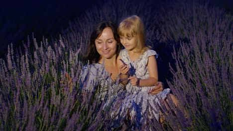 Mother-enjoying-time-with-child-daughter-girl,-touching-sniffing-aromatic-flowers-in-lavender-field