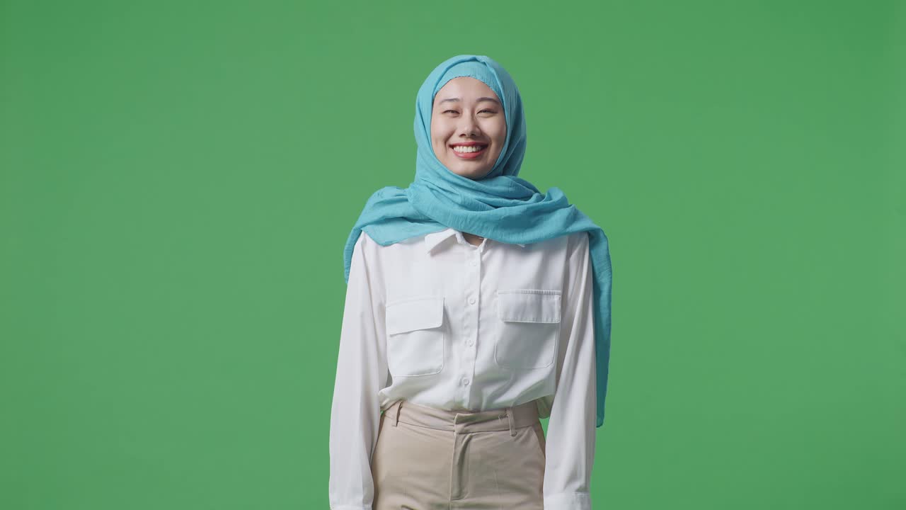 녹색 스크린 배경 스튜디오에 서 있는 동안 카메라를 보고 미소 짓는 아시아 여성