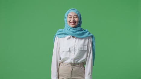 mujer musulmana mirando a la cámara y sonriendo mientras está de pie en el estudio de fondo de la pantalla verde