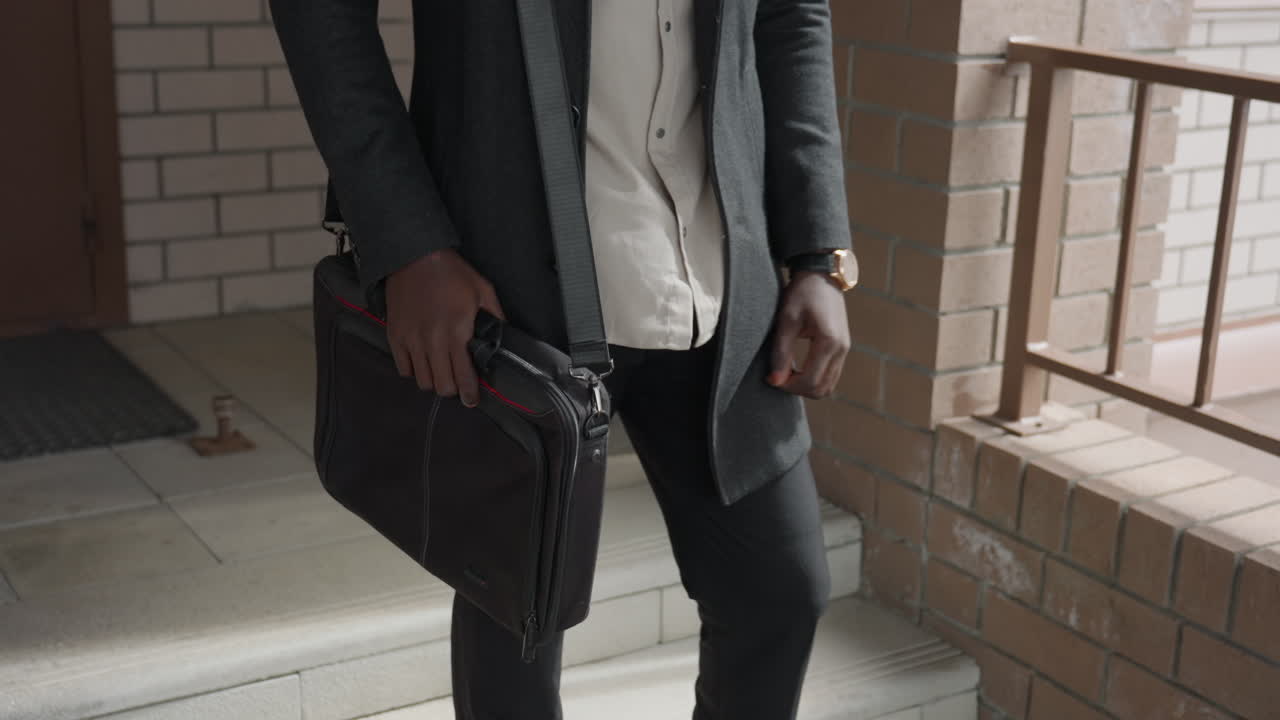 Un joven de piel oscura aminora el paso, mira su reloj de pulsera, escucha el tic tac de la manecilla, calcula los minutos según su horario, camina despacio por el pasillo, mantiene la calma y la concentración bajo la presión del tiempo, con estilo elegante y gestos sutiles.