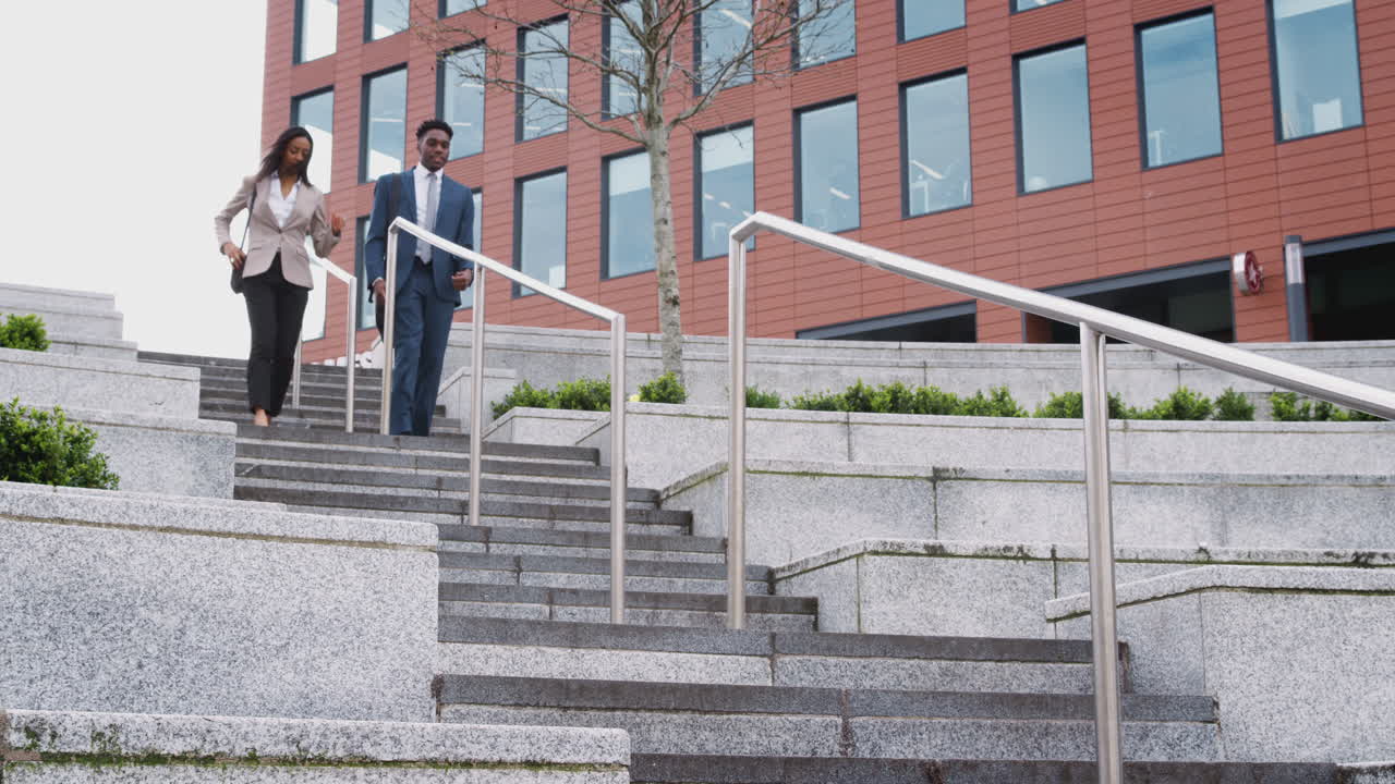 사업가와 사업가 여성이 사무실 건물 밖의 계단을 고 출퇴근하고 있습니다.