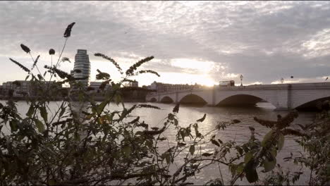 view of london at sunset with a double decker bus driving on the bridge
