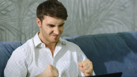 angry man clenching fists in front of computer. annoyed guy working on laptop.