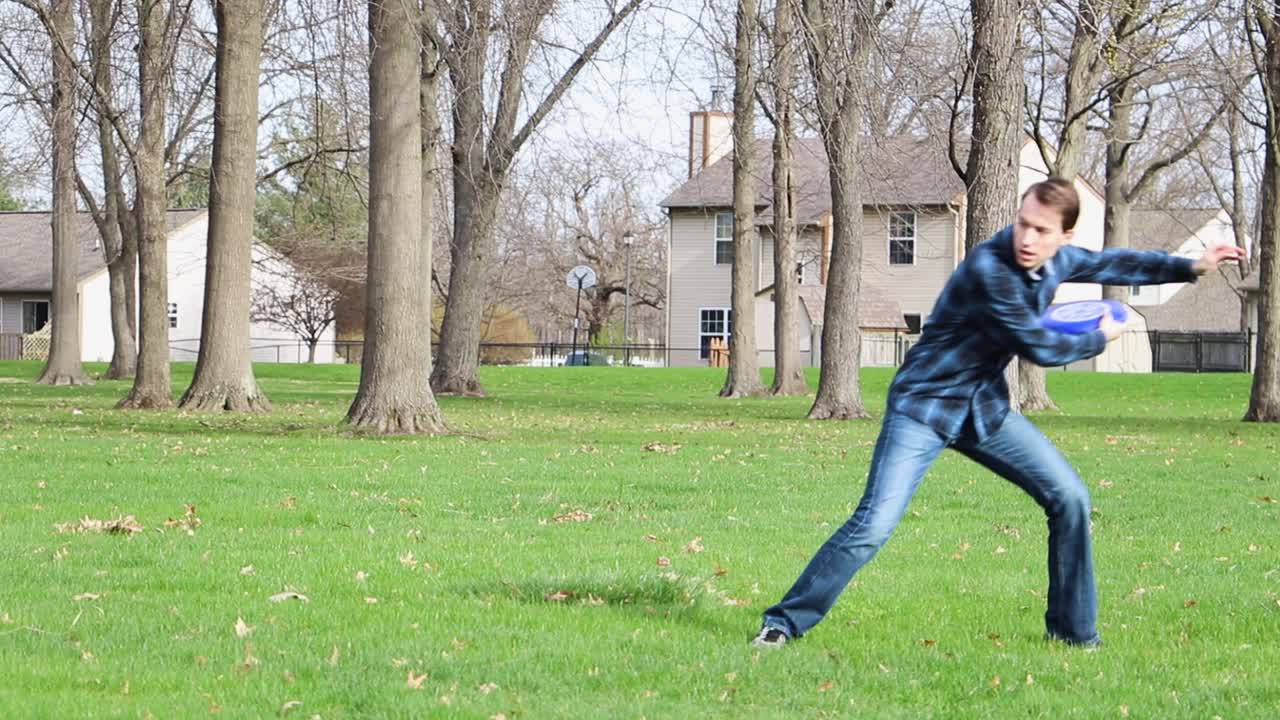 Slow Motion Male Throws Frisbee on the Grass on Sunny Spring Day near trees Clip 2