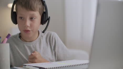 e-learning for school boy at home child is viewing webinar on laptop and writing at copybook language training