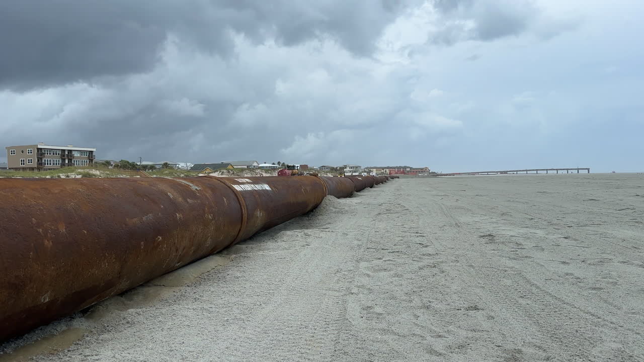 Huge rusty pipe pumping sand from ocean, beach replenishment