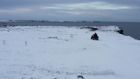 person on atv quad bike riding along rugged snow covered coastal cliffs in iceland