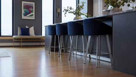 modern kitchen island with blue barstools and wood flooring next to a cozy window seat and artwork
