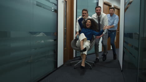 happy employees group celebrating business success racing office chair indoors.