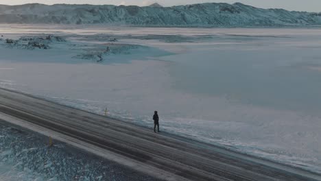 trekker on lonely, icy road in snowy winter iceland landscape - aerial