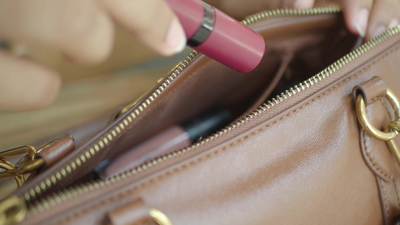 Donna che mette il rossetto in una borsa di pelle marrone