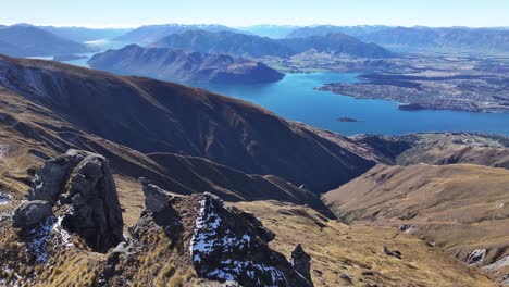 Drone-Volando-Sobre-Rocas-Afiladas,-El-Lago-Wanaka-Y-El-Municipio-En-La-Costa