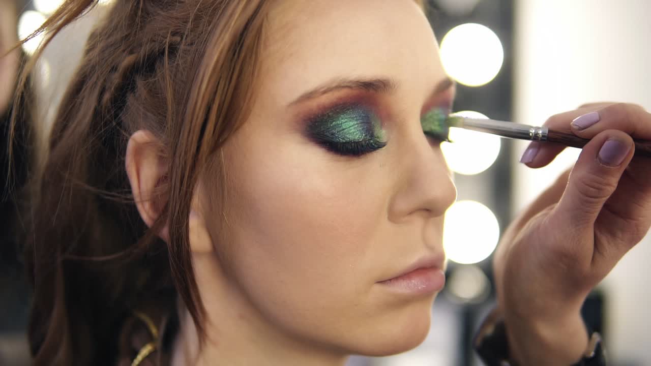 Make-up artist applies some colour shadows on model's eyelids. Side view