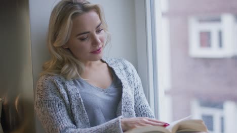 woman reading book near window