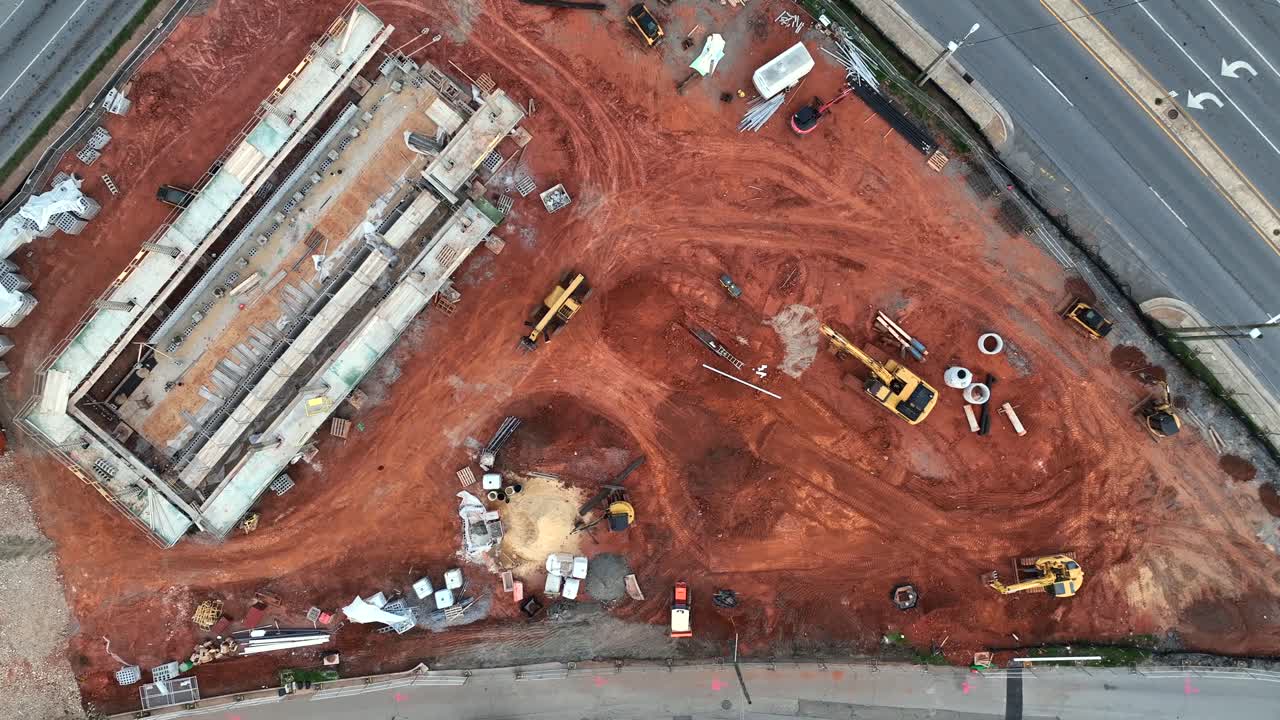 Working excavator and digger on american construction site. Aerial top down shot. Cars driving on street.
