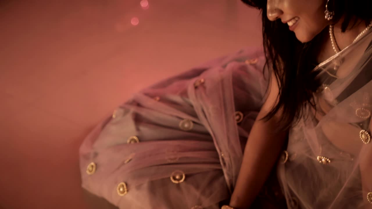 An attractive and smiling woman sitting on the floor in a traditional sari and ornaments drawing a Rangoli with a smile during Diwali festival