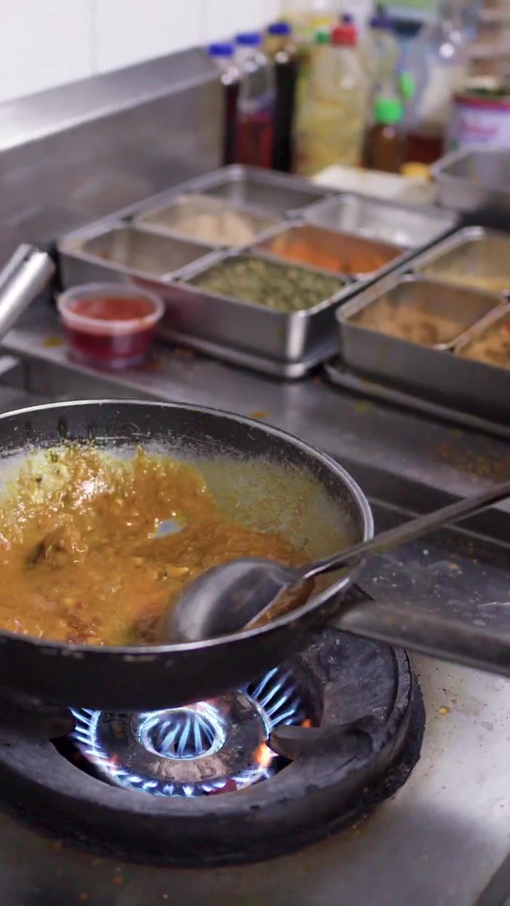 Primo piano di uno chef che mescola curry giallo in un wok su un fornello a gas professionale